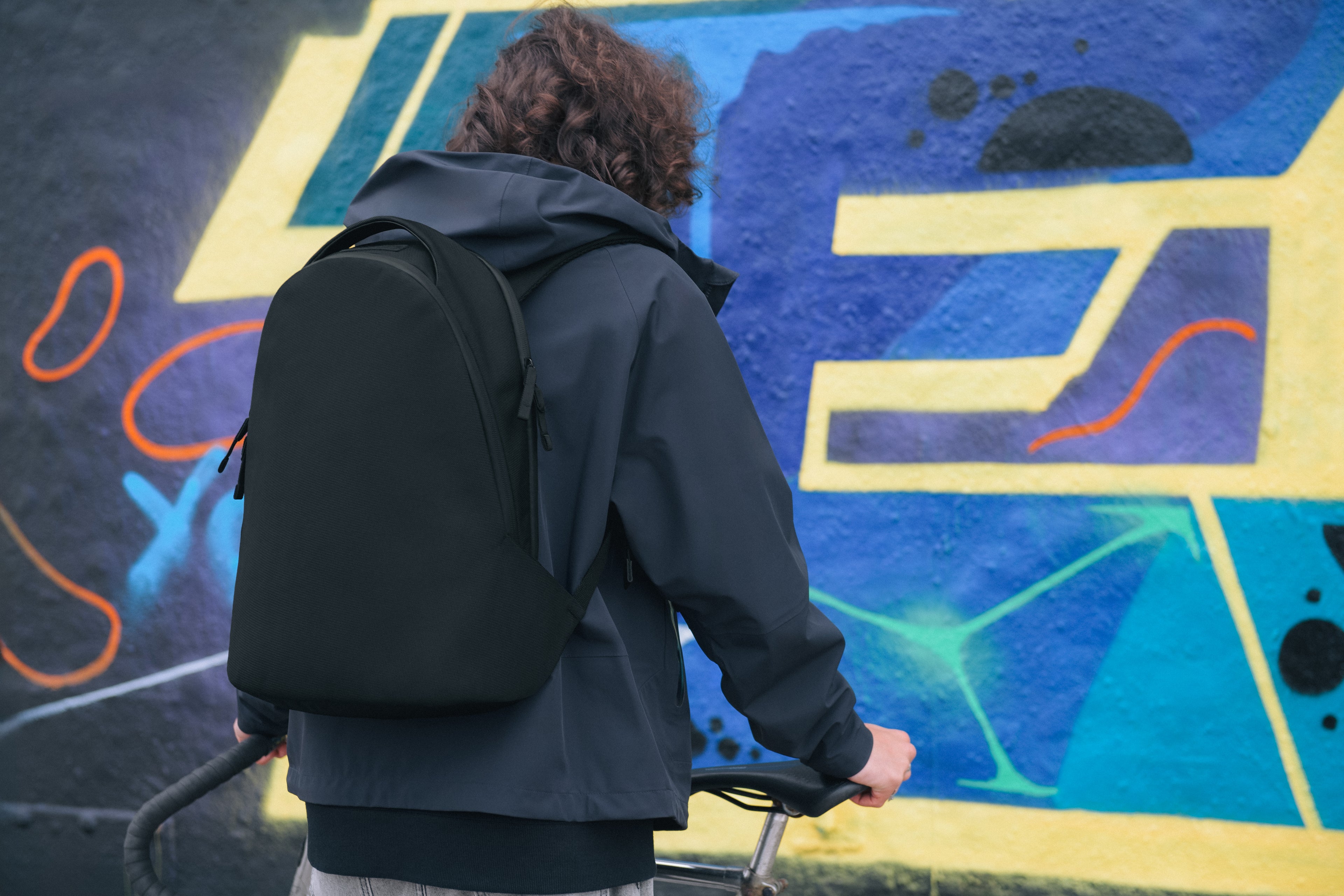 Person with a backpack standing in front of a colorful mural